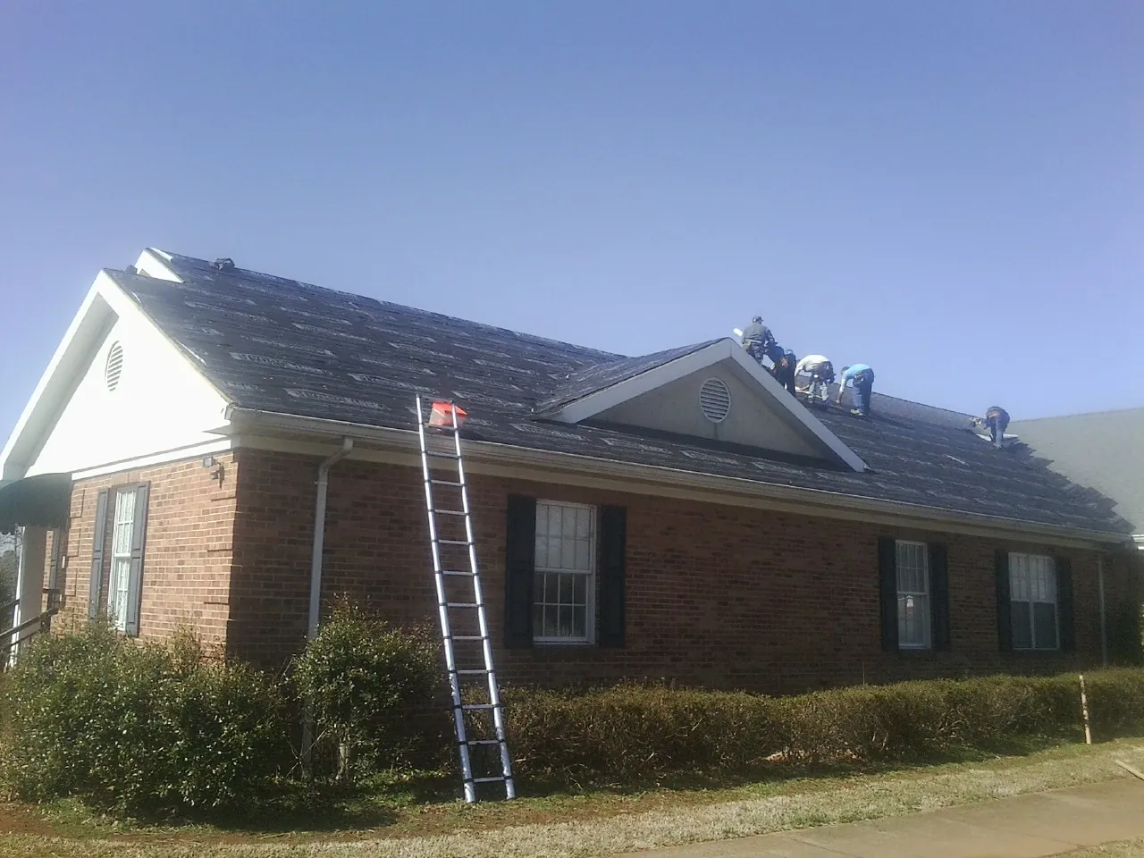 Crew tearing shingles off a brick ranch roof with a ladder set — Emergency Roof Repair work by our crew in Westwood
