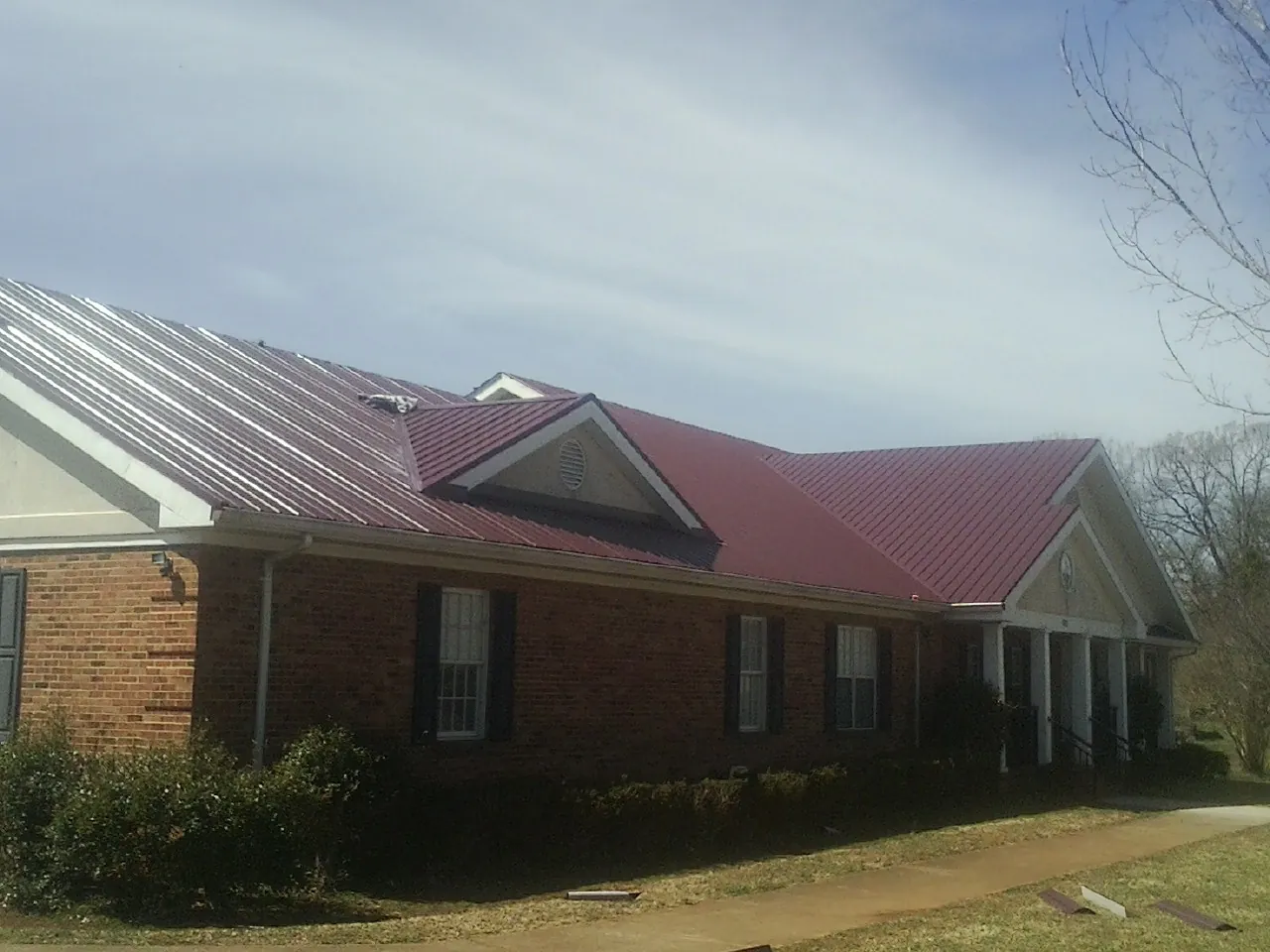 Red metal roof with gabled entries on a long brick building, from a Hail Damage Roof Repair job in Westwood